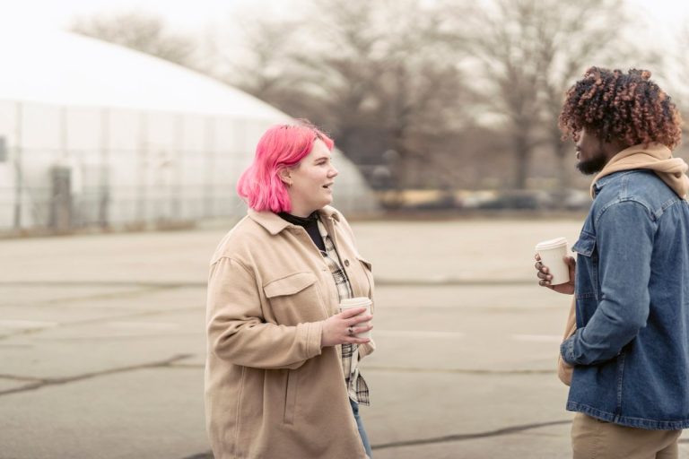 Twee jongeren in gesprek op straat, met koffie in de hand